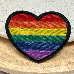 Peut inclure: Un patch en forme de cœur arc-en-ciel avec des rayures rouges, orange, jaunes, vertes, bleues et violettes. Le patch est bordé de noir.