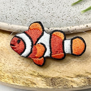 Könnte beinhalten: Ein gestickter Clownfisch-Patch in Orange und Weiß. Der Patch befindet sich auf einem transparenten Hintergrund.