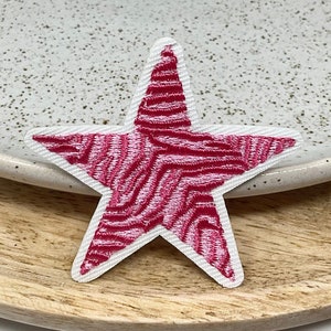 Peut inclure: Un patch en forme d'étoile rose et blanche avec un motif ondulé. Le patch est en tissu et a un contour blanc.