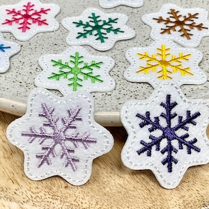 Peut inclure: Huit patchs de flocons de neige en feutre de différentes couleurs, notamment bleu, vert, violet, jaune, marron et rose. Les flocons de neige sont brodés sur du feutre blanc et ont une forme d'étoile.