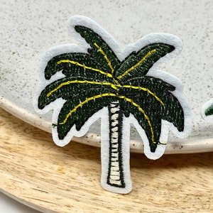 May include: Two embroidered palm tree patches. The larger patch is green with yellow accents and a white trunk. The smaller patch is green with a brown trunk.