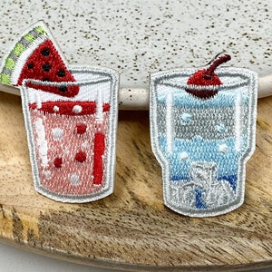 May include: Two embroidered iron-on patches depicting glasses of summer drinks. One patch shows a glass of watermelon juice with a slice of watermelon on top. The other patch shows a glass of a blue drink with a cherry on top.