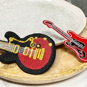 Peut inclure: Deux patchs de guitare brodés. L'un est rouge avec des détails noirs et l'autre est noir avec des détails rouges et dorés.
