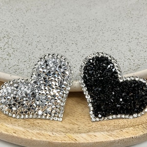 Peut inclure: Deux embellissements en strass en forme de cœur, un argenté et un noir.