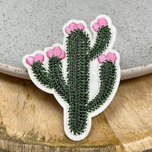 Peut inclure: Un patch brodé de cactus vert avec des fleurs roses. Le patch est sur un fond blanc.