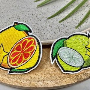 May include: Two embroidered iron-on patches featuring a yellow lemon with a green leaf and a red grapefruit slice, and a green lime with a white slice and a yellow star.