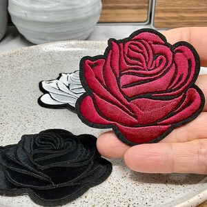 Peut inclure: Trois patchs brodés thermocollants de roses en noir, blanc et rouge.