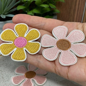 May include: Three embroidered flower patches in yellow, pink and brown. The patches are in the shape of a daisy with a circle in the centre.