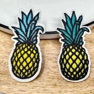 Peut inclure: Deux patchs brodés en forme d'ananas avec des fruits jaunes et des feuilles bleues et vertes.