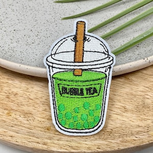 Peut inclure: Patch brodé représentant un bubble tea vert sur fond blanc avec une paille brune. Le patch est brodé avec les mots "Bubble Tea".