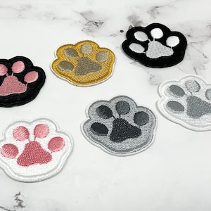 Peut inclure: Écussons brodés en forme de pattes de chat, de différentes couleurs : noir et rose, or et gris, noir et blanc, blanc et rose, gris et gris foncé, et blanc et gris. Idéal pour personnaliser vêtements et accessoires.