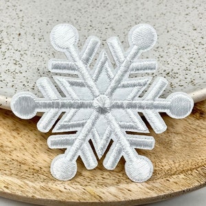 Può includere: Toppa ricamata a forma di fiocco di neve bianco. Il fiocco di neve è un simbolo tradizionale delle festività invernali.