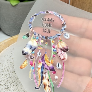 May include: A white dreamcatcher with colourful feathers and beads. The dreamcatcher has the text "Dreams Come True" written on it.