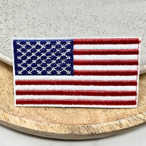 Peut inclure: Un patch brodé du drapeau américain, rouge, blanc et bleu. Le patch est sur une surface en bois.