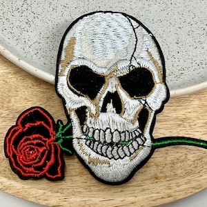 Peut inclure: Crâne brodé blanc avec une orbite noire et une rose rouge avec une tige verte dans sa bouche.