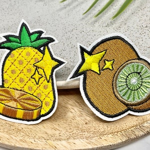 Peut inclure: Deux patchs brodés à repasser représentant un ananas et un kiwi. L'ananas est jaune avec un sommet vert et une tranche d'ananas en bas. Le kiwi est brun avec un centre vert. Les deux patchs ont des étoiles jaunes.