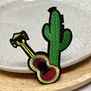 Peut inclure: Un patch brodé représentant un cactus vert et une guitare rouge, jaune et noire. Le patch est parfait pour ajouter une touche de style sud-ouest à vos vêtements, sacs ou autres accessoires.