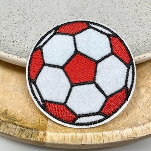 Peut inclure: Un écusson de football brodé blanc et rouge. L'écusson est rond et a un contour noir.