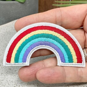 May include: A rainbow-colored embroidered patch with a white background. The rainbow has red, orange, yellow, green, blue, indigo, and violet stripes.