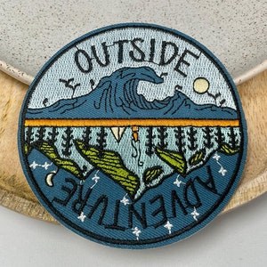 Peut inclure: Un patch brodé bleu et vert avec le texte "OUTSIDE ADVENTURE" en cercle. Le patch représente une chaîne de montagnes, une vague, un croissant de lune et des étoiles.