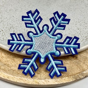 Peut inclure: Patch brodé en forme de flocon de neige bleu et blanc avec une étoile à six branches au centre.