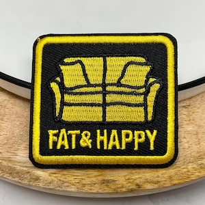Peut inclure: Écusson brodé avec un fond noir et une bordure jaune. Le patch présente un motif de canapé jaune et les mots "FAT & HAPPY" en lettres blanches.