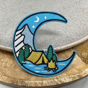 Peut inclure: Un patch brodé en forme de croissant de lune bleu avec une scène de camping. La scène comprend une tente jaune, des arbres verts, un feu de camp et une chaîne de montagnes. La lune a un croissant de lune blanc et une étoile blanche.