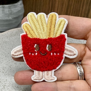 Könnte beinhalten: Ein roter und gelber Filz-Aufnäher mit einem Cartoon-Pommes-Charakter mit einem lächelnden Gesicht und Armen.