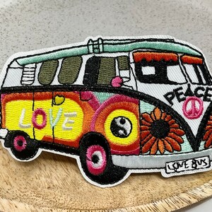 Könnte beinhalten: Gestickter Aufnäher eines bunten, alten Volkswagen-Busses mit den Worten "Love" und "Peace" an der Seite. Der Bus hat ein Peace-Zeichen, Blumen und ein Yin-Yang-Symbol. Der Aufnäher trägt auf der Rückseite die Aufschrift "Love Bus".