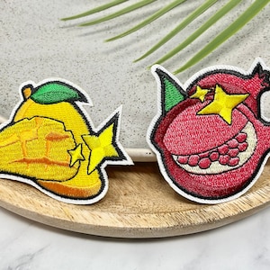 May include: Two embroidered iron-on patches, one of a yellow mango with a star and the other of a red pomegranate with a star.