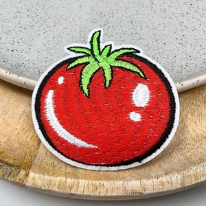May include: Red embroidered tomato patch with a green stem and white details.