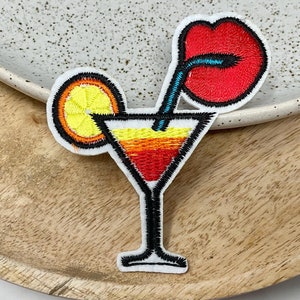 May include: Embroidered iron-on patch featuring a cocktail glass with a red, orange, and yellow drink, a lemon wedge, and a straw with a red lip on top.