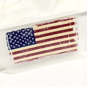 Peut inclure: Un autocollant rectangulaire représentant le drapeau américain avec un aspect vieilli et vintage. Le drapeau présente des rayures rouges et blanches, un champ bleu avec des étoiles blanches et un aspect légèrement usé.