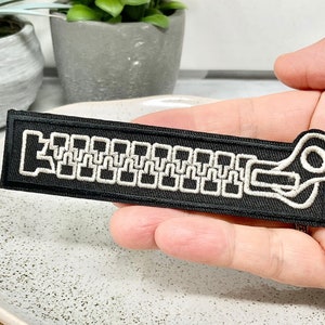 Peut inclure: Un patch thermocollant noir avec un motif de fermeture éclair brodé en blanc.