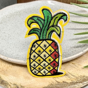 May include: A yellow pineapple embroidered patch with green leaves and a red and yellow checkered pattern.