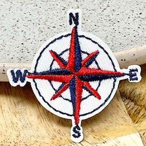 Peut inclure: Un écusson de boussole brodé blanc avec une rose des vents rouge et bleue. Les points cardinaux sont étiquetés N, S, E et W.