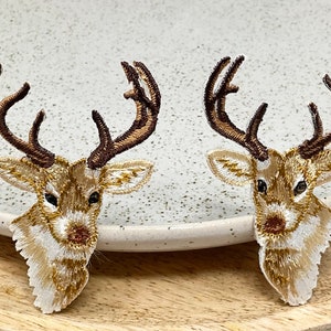 May include: Two embroidered iron-on patches of brown and white deer heads with antlers.