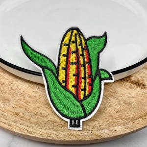 May include: Embroidered iron-on patch of a yellow and red corn cob with green leaves.