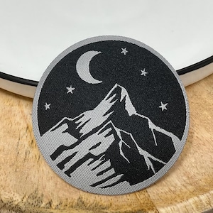 May include: A grey and black embroidered patch featuring a crescent moon and stars above a mountain range.