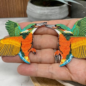 May include: Two embroidered iron-on patches of kingfishers, one facing left and one facing right. The birds are orange, yellow, green, and blue.