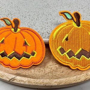 May include: Two orange felt pumpkin patches with embroidered details. The pumpkins have a yellow and brown face with a toothy grin.