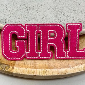 May include: Pink felt applique with the word "GIRL" in white stitching.