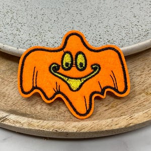 Peut inclure: Fantôme en feutre orange avec un contour noir et un visage souriant jaune. Le fantôme est une décoration d'Halloween.