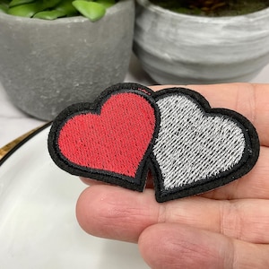 May include: Two embroidered felt hearts, one red and one silver, sewn together. The hearts are outlined in black thread.