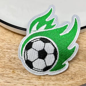 Peut inclure: Patch brodé vert et blanc d'un ballon de football en feu. Le ballon de football est blanc avec des coutures noires et les flammes sont vertes.