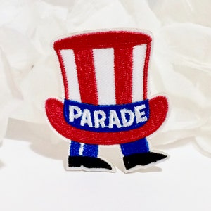 Peut inclure: Patch en feutre rouge, blanc et bleu d'un dessin animé d'Oncle Sam portant un chapeau haut de forme avec le mot "PARADE" sur le bandeau du chapeau.