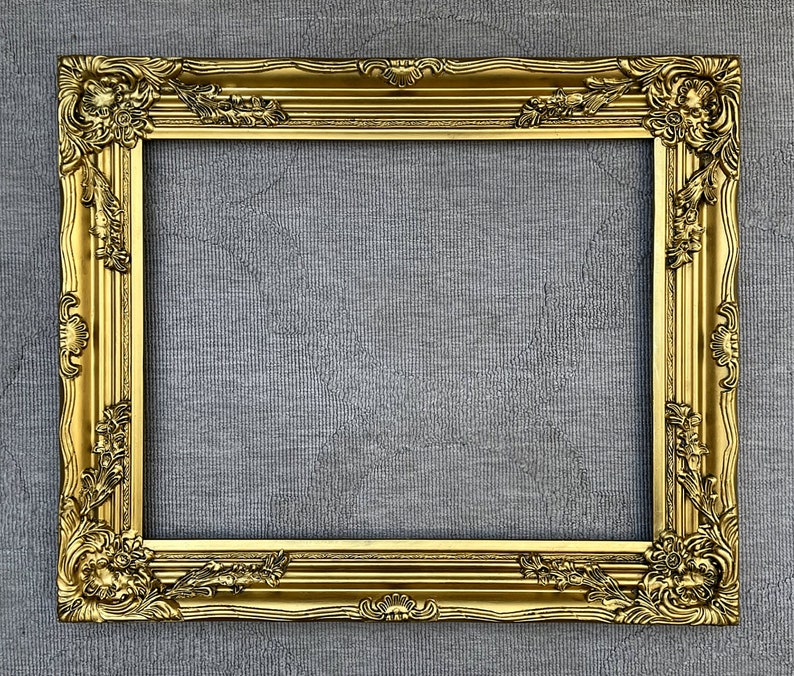 May include: A gold ornate picture frame with a detailed design. The frame is empty and ready for a picture.