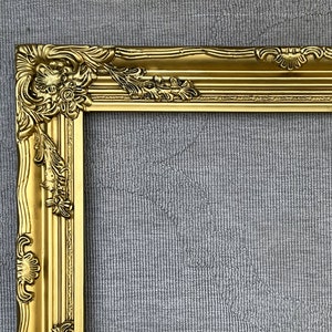 May include: A gold ornate picture frame with a detailed, intricate design. The frame is made of wood and has a glossy finish.