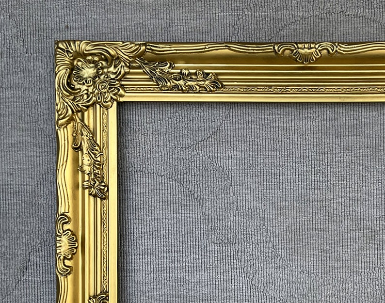 May include: A gold ornate picture frame with a detailed, intricate design. The frame is made of wood and has a glossy finish.