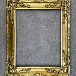 May include: A gold ornate picture frame with intricate carvings and a raised edge. The frame is against a gray textured background.